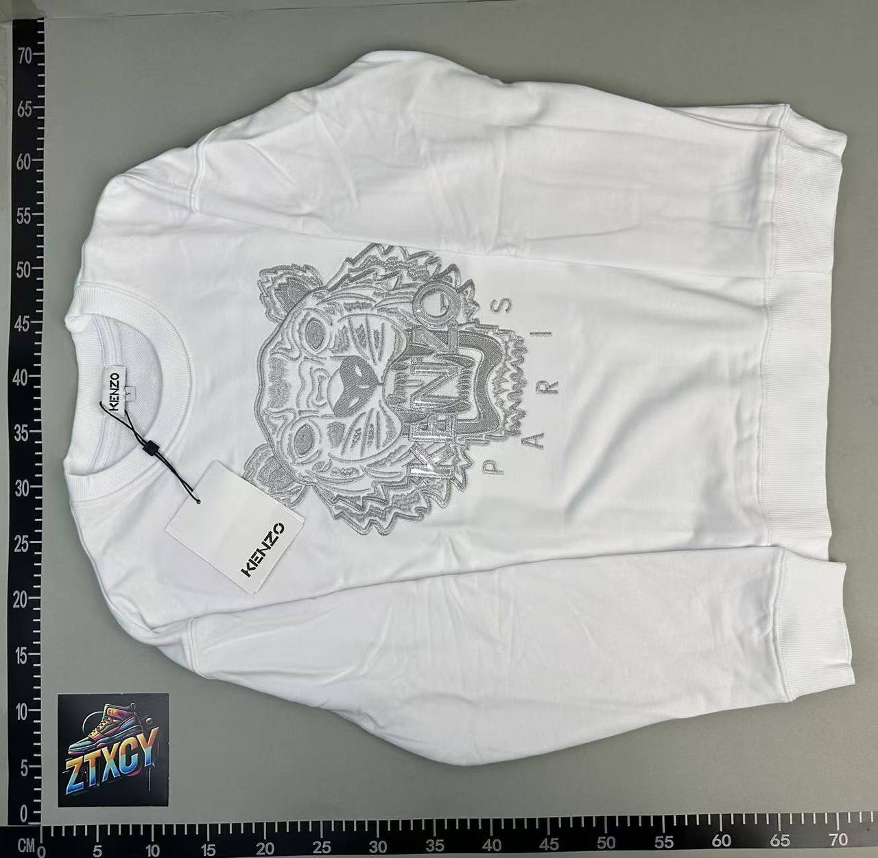 White crewneck laid on a warehouse measurement board for approximate overall sizing